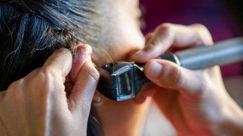 A doctor's ear inspection device placed in the right ear on a woman's head