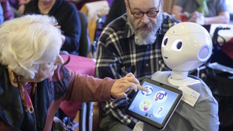 An elderly resident looks to a robot called "Pepper" during a presentation of two robots at the August-Stunz-Altenzentrum senior care facility.