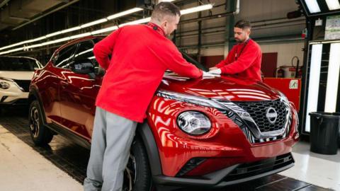 Two workers wearing red tops standing by a red Nissan Juke car on the production line at Nissan's plant in Sunderland