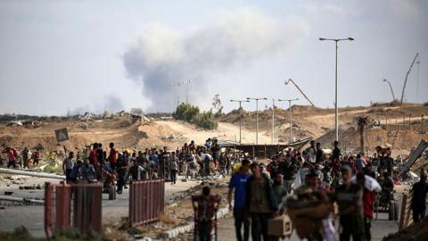 A plume of smoke rises in the background as Palestinians return from a food distribution point run by the US and Israeli-backed Gaza Humanitarian Foundation (GHF) group. 