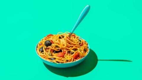 A bowl of pasta in a tomato based sauce with black olives visible and a fork sticking out of it. 