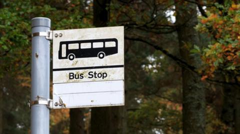 A generic bus stop sign. The sign is attached to a grey metal pole. The sign is square shaped and shows a black silhouette of a bus and the words "bus stop".