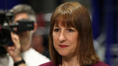 Chancellor Rachel Reeves looks down and a camera can be seen behind her, filming. 