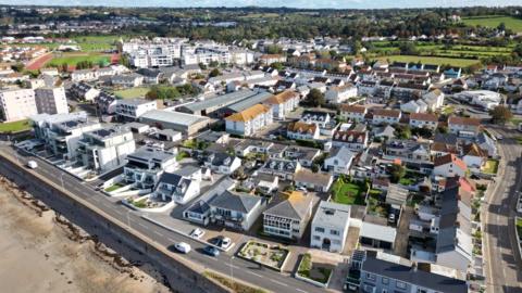A photo from a drone showing houses, a road, the edge of a beach and a sports field in Jersey