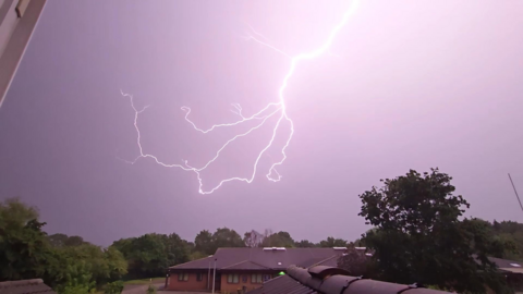 A lightning strike lights up the night sky, which looks purple against the bright lightning.