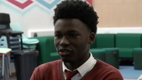 Pupil Lanre in school in a dark red school jumper and tie.