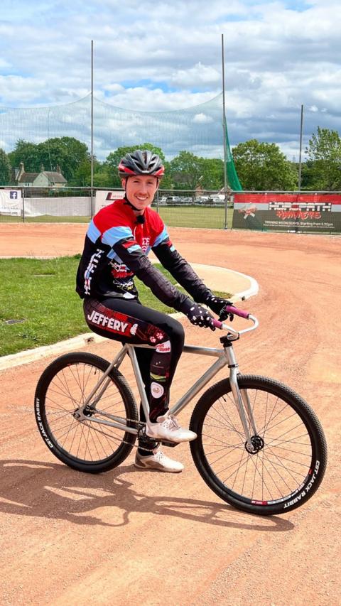 Man sits facing on a bike facing the camera. He is on a cycle speedway track.