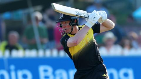 Cameron Bancroft batting for Gloucestershire. He is wearing a helmet, and the black and yellow kit, and holding a cricket bat.
