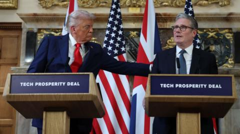 US President Donald J. Trump and British Prime Minister Keir Starmer stand behind a lectern each at a press conference, with USA and British flags behind them.