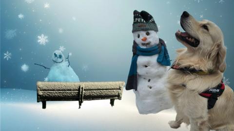 A snowy scene with a snow covered bench, snowmen and a dog. 