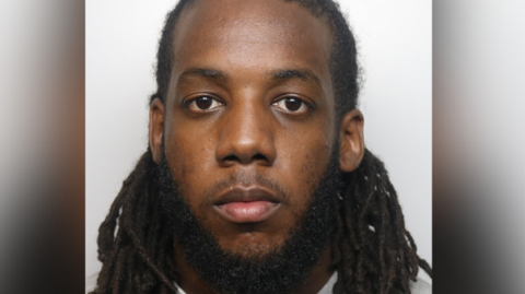 Kyrie Gruber mugshot. He has long dreadlocked hair and a large dark beard.