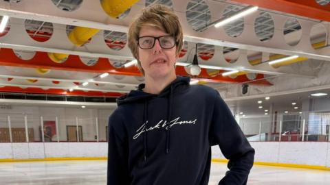 A man wearing a blue hoodie in an ice skating rink