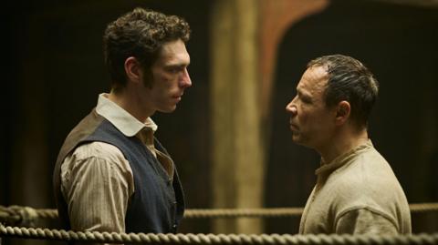 Publicity picture for A Thousand Blows. It shows Nelson-Joyce (left) stood in a boxing ring facing each other. Nelson-Joyce wears a striped-shirt under a blue waistcoat and has curly dark hair. Graham wears a beige top and has short dark hair.