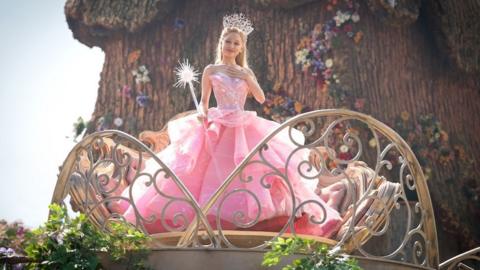 Ariana Grande wears a pink gown complete with a crystal embellished crown and wand.