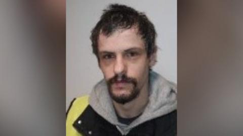 Billy Ingram: A man who is wearing a grey hoodie with a black coat over the top. He has dark facial hair and is looking directly at the camera.