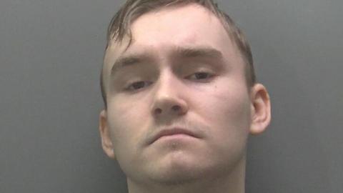 Max Roberts's head and shoulders in his custody photo. He has short fair-coloured hair and is wearing a grey top.