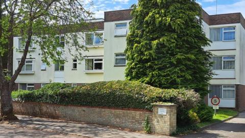The outside of the Wimborne House flats a white building made up of three floors with trees outside