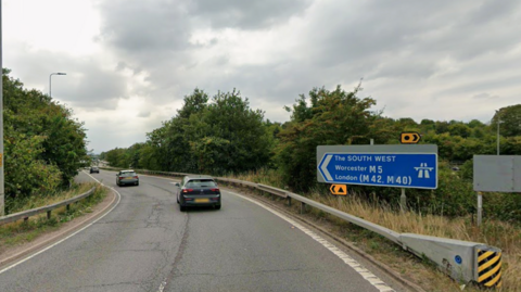 A motorway slip road on a cloudy and grey day. A blue sign reads The South West, Worcester M5, London M42, M40. 