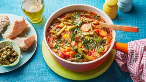 A red bowl of a tomato and green bean mixture on a blue surface
