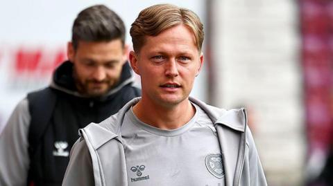 Frankie Kent walks into a stadium in his pre-match grey kit 