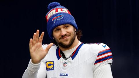 Buffalo Bills quarterback Josh Allen waves while wearing the team uniform and a Bills woolly hat