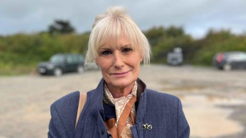 Catherine jones looking at the camera wearing a smart overcoat. She has blonde hair