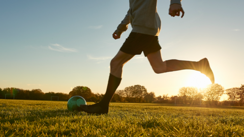 A boy runs across a field with a football