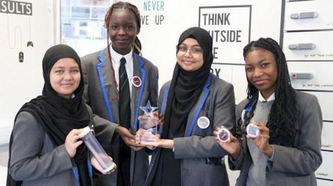 [L-R - Tajkia (14), Neveah (15), Sabriha (15), Daniela (15) ] Pupils pictured in grey school uniform hold a trophy and badges