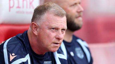 Mark Robins leans forward on his seat in the Stoke City dugout during a game 