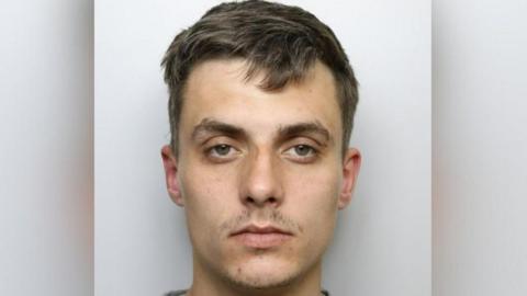Custody shot of Regan Kemp. He has short brown hair, has a serious expression and is stood in front of a grey background. 