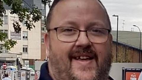 A smiling man with glasses stood on a high street