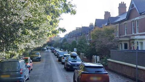 Street view image of Cleveland Road, a row of red brick houses to the right and trees to the left, with cars parked either side