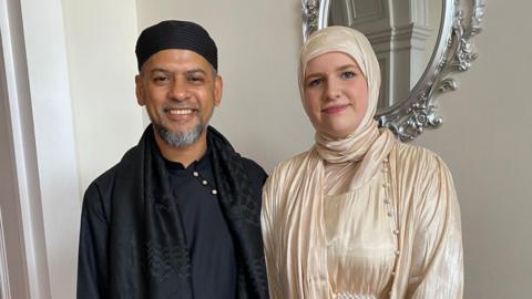 Mohammed Ali wearing all Black as he stands next to his daughter Aleyah, who is wearing a silk hijab and dress.