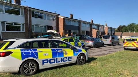 Three Wiltshire Police cars outside red brick houses in a residential area of Wilton