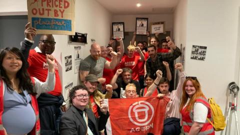 Residents many wearing red Acorn community union tops protest against rent increases with some holding a red Acorn flag and placards. 