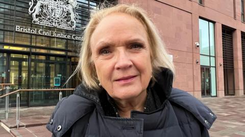 Beverley Watkins, managing partner of Watkins Solicitors in Bristol. She has blonde hair and is wearing a grey coat, standing outside the Bristol Civil Justice Centre.