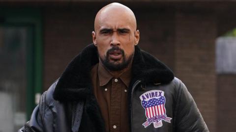 Ashley Warren outside court wearing a brown shirt and a black leather jacket. He is scowling at the camera.