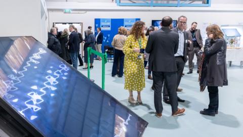 A large solar panel seen leaning on a stand, as people talk in groups in the background at the opening of the new green skills centre.