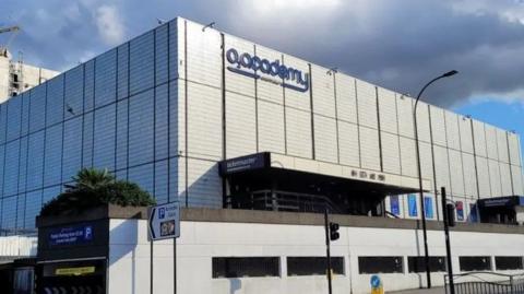 The exterior of the O2 Academy Sheffield building. It is a flat, white-ligh grey building. There are steps up to the entrance.