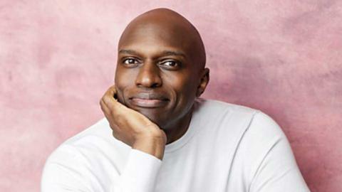 A man in a white top looking at the camera and smiling