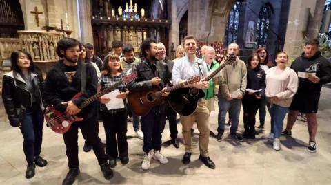 A choir rehearsing in Newcastle Cathedral  with three people at the front holding choirs 