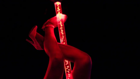 A view of a woman's legs wrapped around an illuminated pole in the dark at a lap-dancing club.