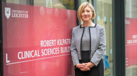 Consultant Gynaecological Oncologist, Dr Esther Moss, stood next to a sign for the University of Leicester