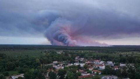 A drone view showing the Sainte-Helene commune in France with smoke rising in the background during a wildfire in a forest area in Saumos
