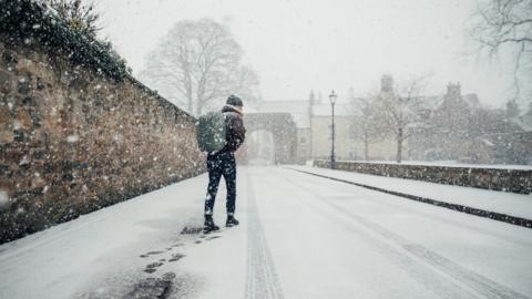 Man walks along a snow covered street with a rucksack on his back 