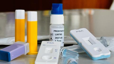 Unused medical equipment for rapid PSA testing including two yellow lancets used to pierce the skin, a small bottle of clear chemical regent used for the test and two white testing cassettes, labelled PSA, which closely resemble the lateral flow tests used in the Covid pandemic.