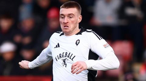 Ryan Watson on the ball for Salford City with his arms out.