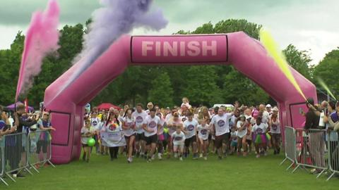 Hundreds of runners in white t-shirts set of on a run under a huge purple  inflatable archway with coloured powder in the air above it