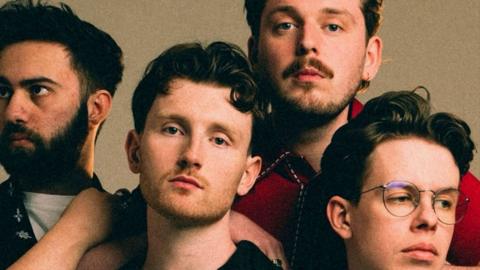 Four male members of a band. Two have beards and one is wearing glasses