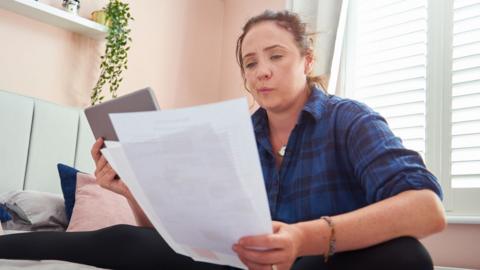 Woman sits on bed looking at papers 